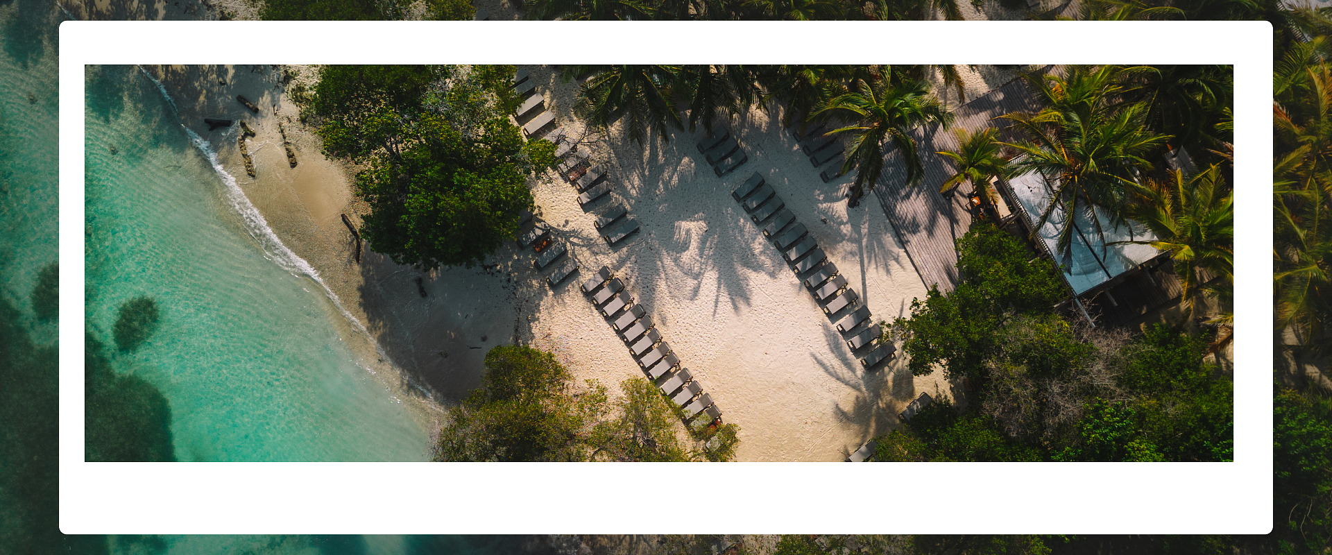 Stunning aerial view of a paradisiacal private island with turquoise waters, overwater bungalows, and white sand. Discover our 15% discount offer on all romantic plans
